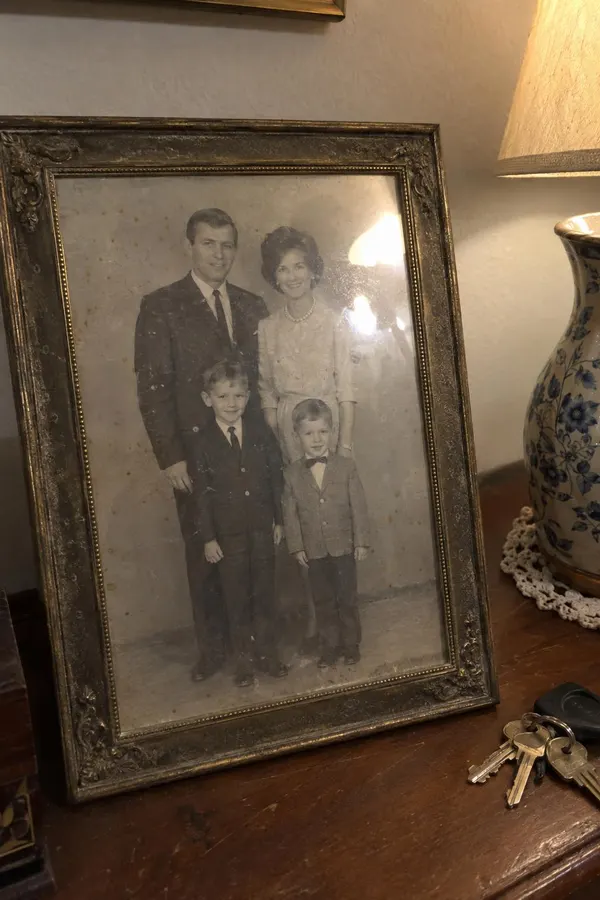 A phone photo of an old print, in a frame: a 1960s family portrait of parents and two small boys